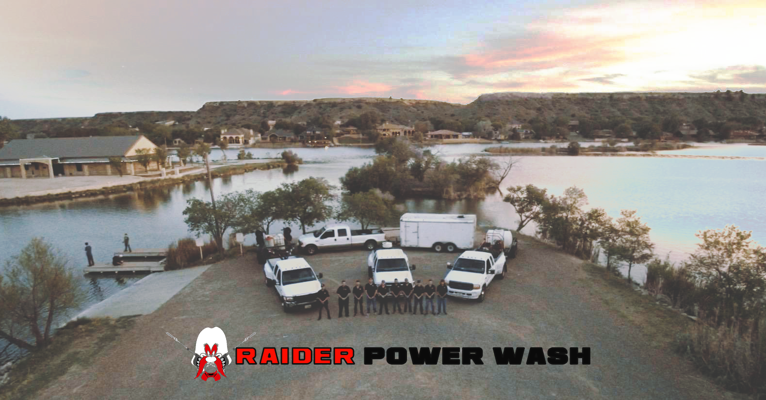 A crew of professional vent hood cleaning technicians in black shirts posing in front of 4 white trucks with various commercial power washing trailers attached in front of a lake at sunset
